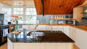 A modern kitchen with a granite countertop, stainless steel sink, and wooden ceiling. - Hepple Hill Cottage (Consett)