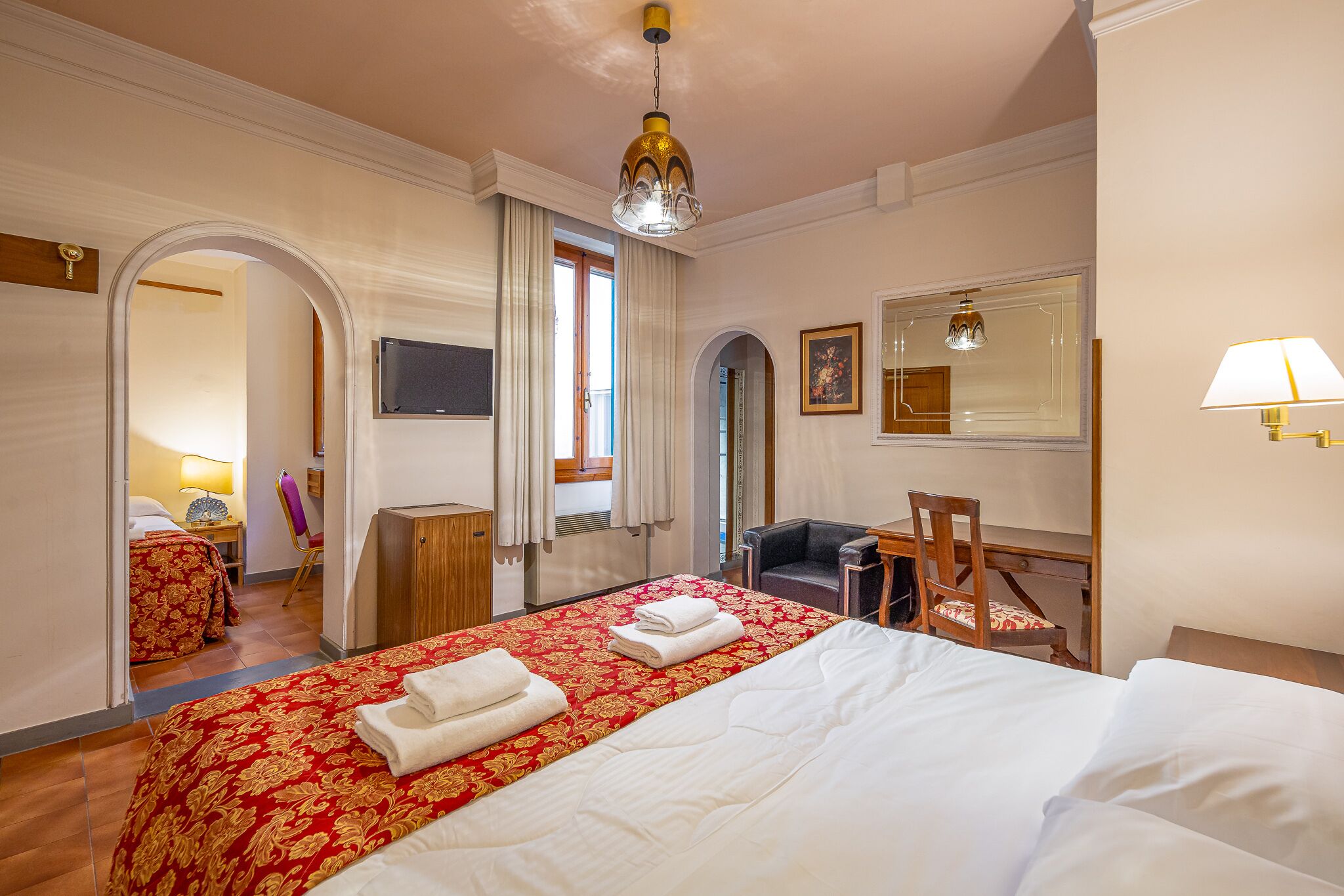 Ein Hotelzimmer mit einem großen Bett, einem Schreibtisch, einem Sessel und einem Fernseher.