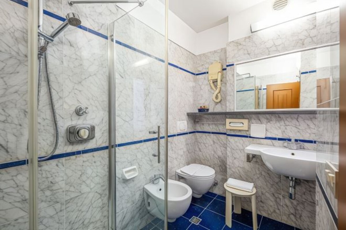A modern bathroom with a glass shower enclosure, a white sink, a toilet, and a bidet.