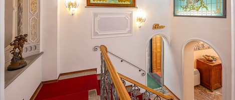 A grand staircase with red carpet, ornate wall decorations, and a chandelier.