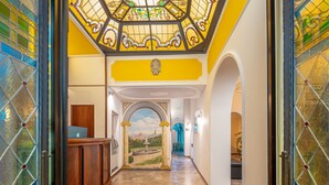 Un pasillo con un mostrador de recepción de madera, un mural de un paisaje y un techo de vitral.