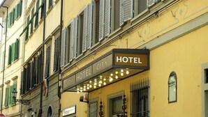 Un hotel con fachada amarilla, contraventanas verdes y un cartel que indica que es un hotel urbano.