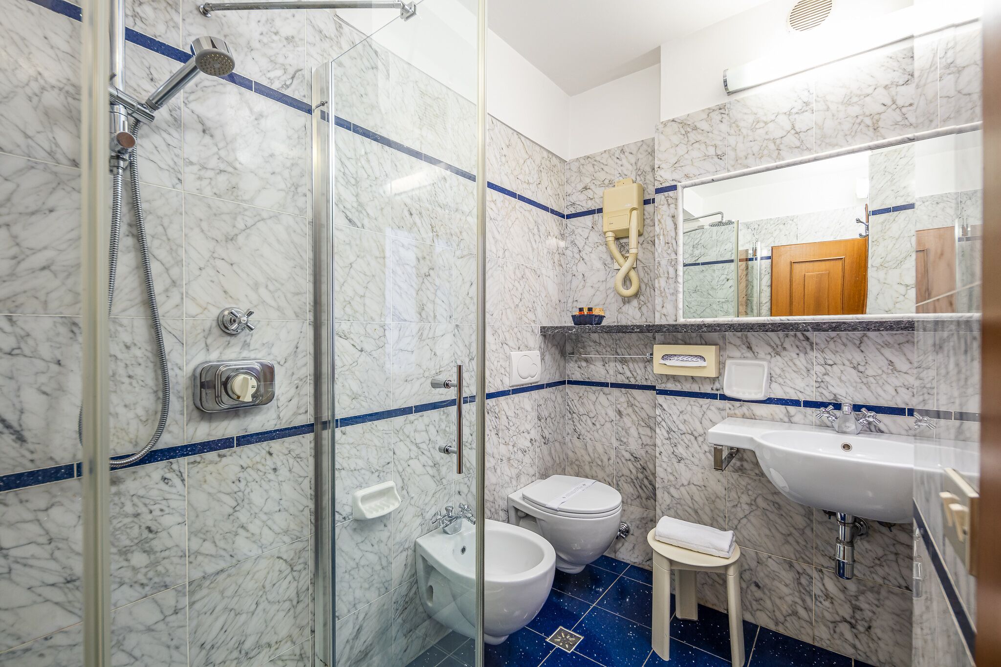 Een moderne badkamer met een douche met glazen wand, een toilet, een wastafel en een bidet.