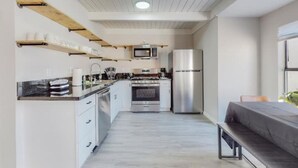 Une cuisine compacte avec des meubles blancs, un four encastré, un four à micro-ondes et un réfrigérateur. On y trouve également un banc et une petite table dans l’espace repas.