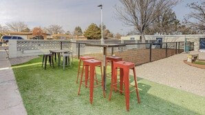 Un espace extérieur aménagé avec une table et quatre tabourets, entouré d’une clôture et d’une pelouse.