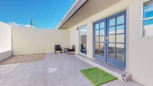 Eine Terrasse im Freien mit befestigtem Boden, zwei Stühlen und einer kleinen Fläche aus Kunstgrün.
