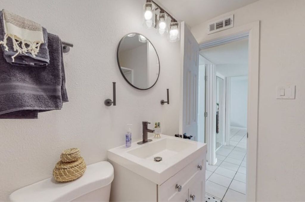 Une salle de bain avec un lavabo blanc, un miroir rond et un porte-serviettes sur lequel est posée une serviette pliée.