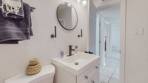 Ein Badezimmer mit einem weißen Waschbecken, einem runden Spiegel und einem Handtuchhalter mit einem gefalteten Handtuch.