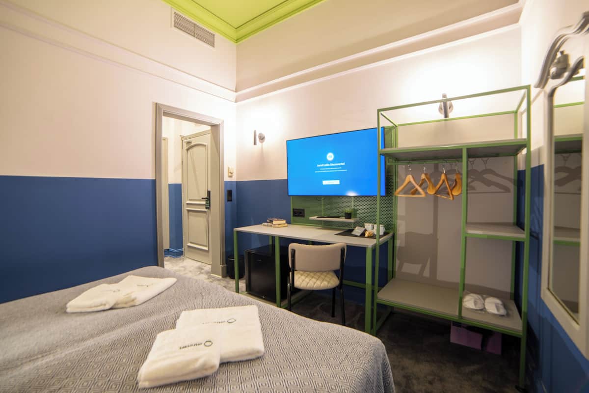 A hotel room with a bed, a desk, a chair, a TV, and a wardrobe.