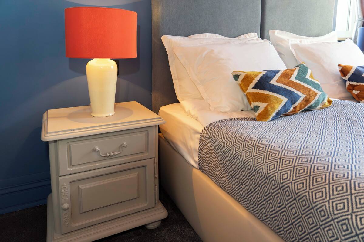 A neatly made bed with patterned bedding, a bedside table with a lamp, and a nightstand with drawers.
