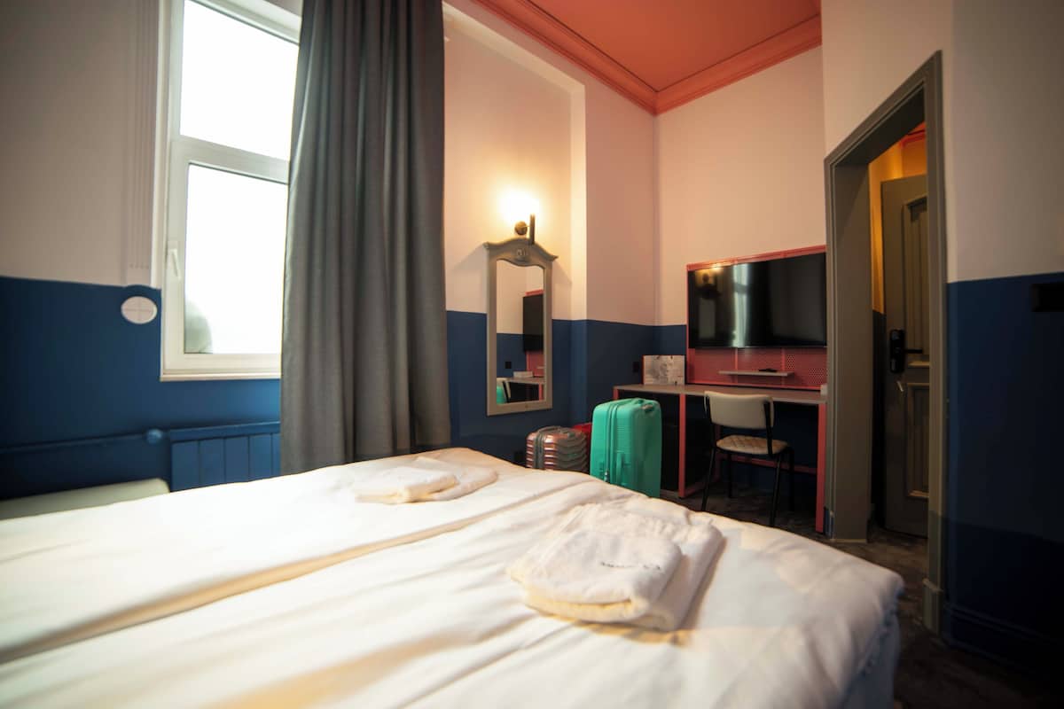A hotel room with two beds, a desk with a chair, a television, and a mirror.