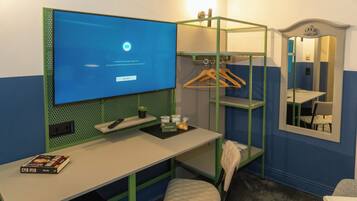 A hotel room with a desk, a chair, a hanging clothes rack, a mirror, and a television displaying a blue screen.