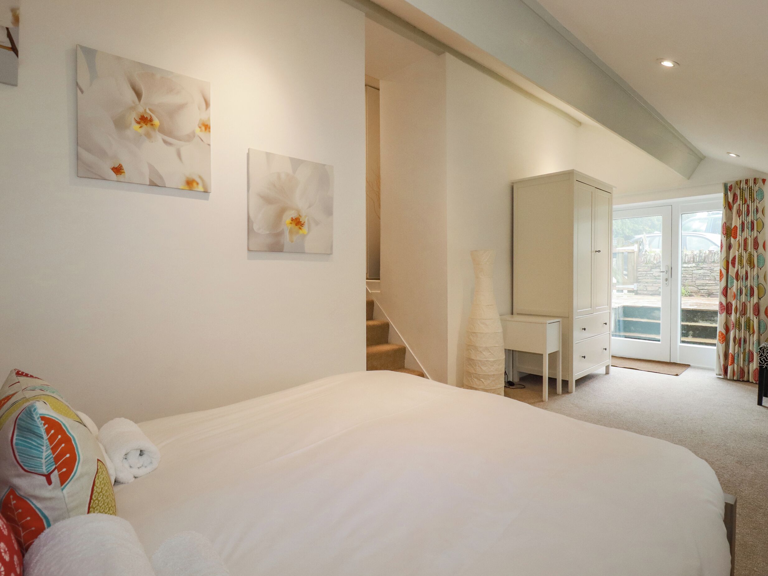 A bedroom with a large bed, a dresser, and a desk. There are two paintings on the wall and a window with curtains.