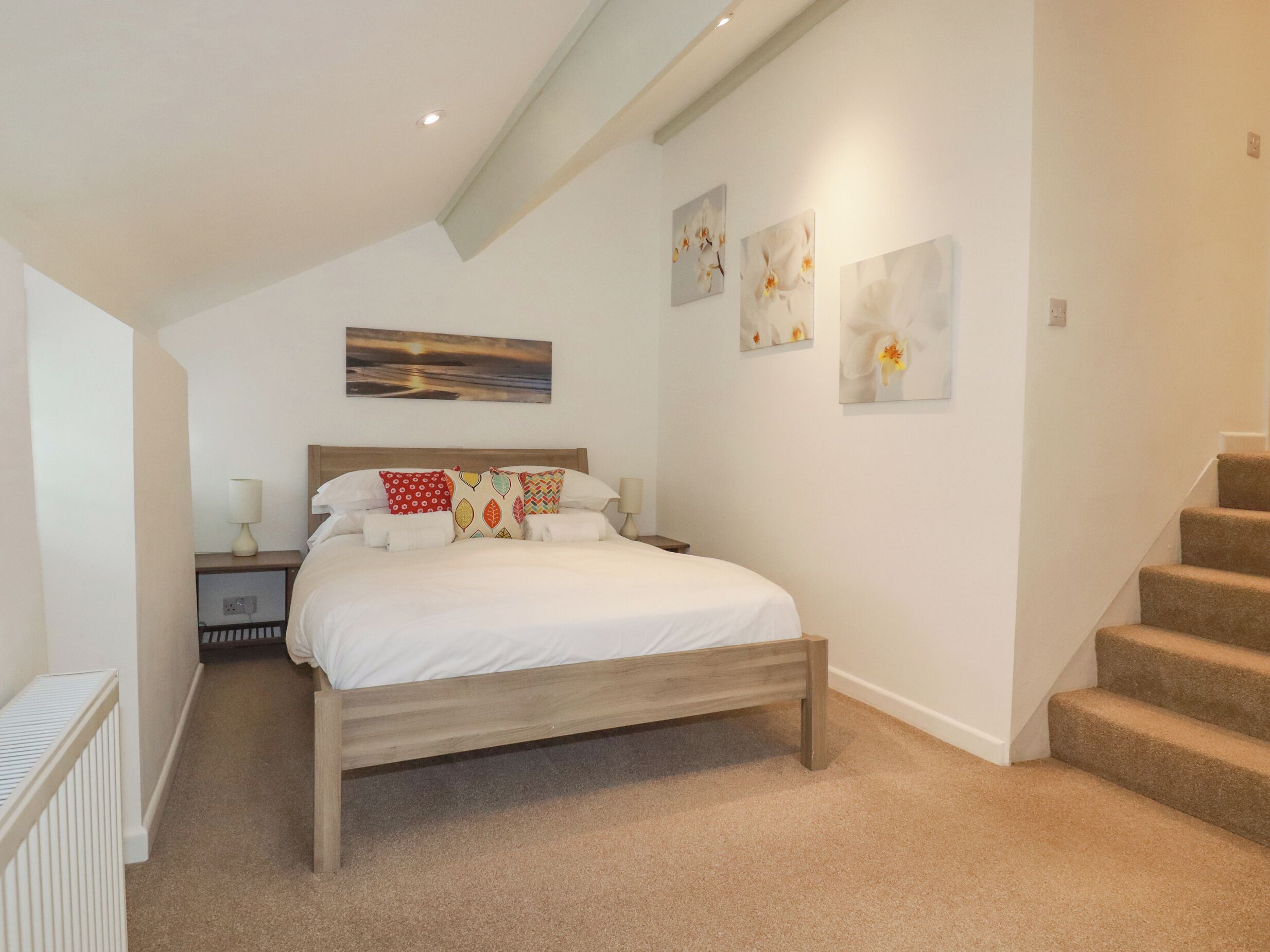 A bedroom with a wooden bed, white bedding, a nightstand, and a wall-mounted lamp.
