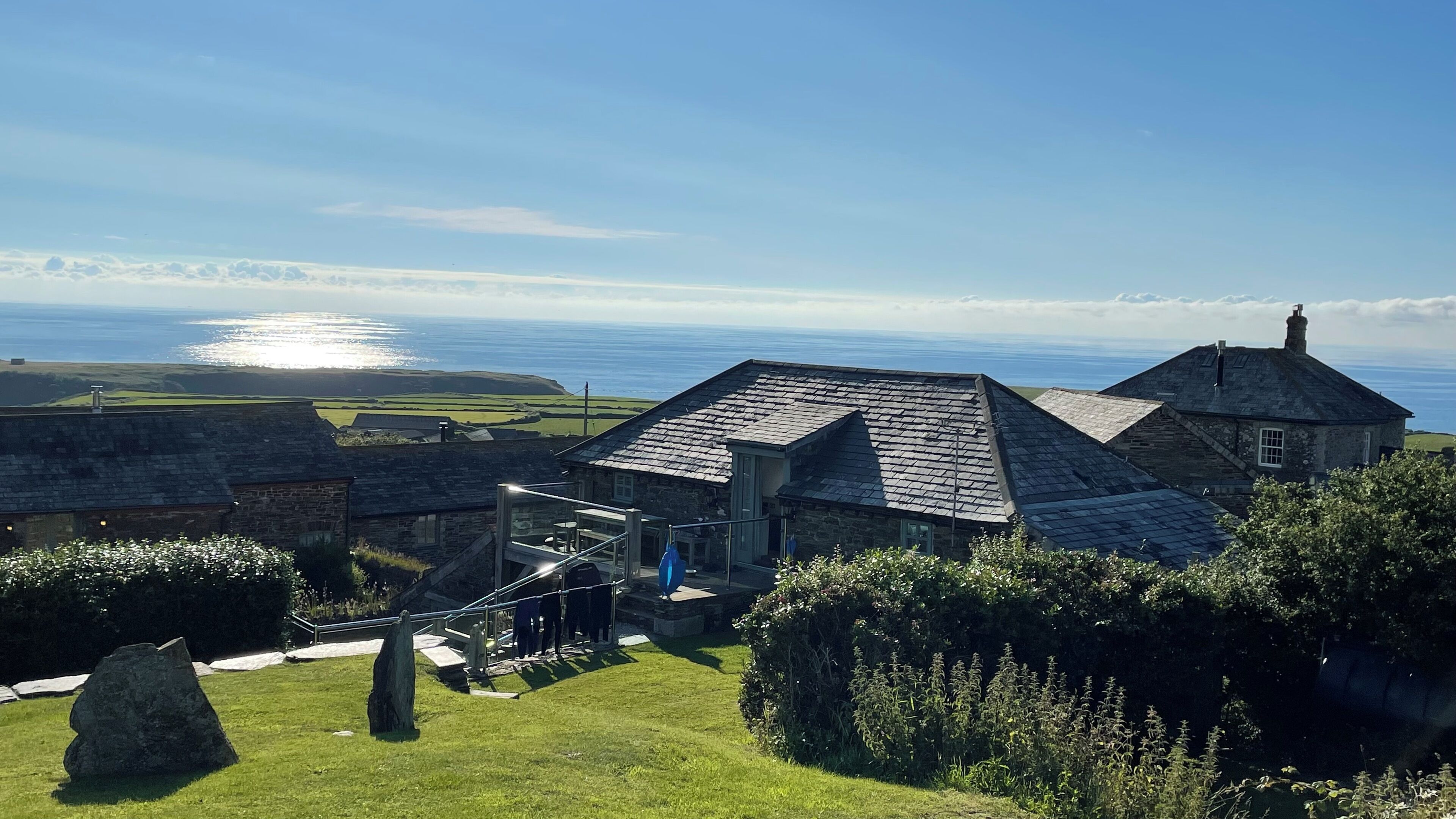 A stone building with a steep roof, a staircase leading to a door, and a view of the sea.