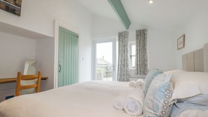 Quarto com cama, uma cadeira, janela com cortinas e vista para o exterior.