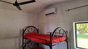 A bunk bed with red bedding in a room with white walls, a ceiling fan, an air conditioning unit, and a window with a view of greenery. - Casa de Playa con Mini Golf (La Libertad Department)