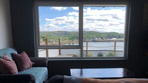A room with a large window offering a view of a dock and hills. There is a bed with a patterned bedspread and pillows, and a small table with a water glass. - 2 bed apartment, waterfront views, 5 mins from shops & restaurants (Lochinver)