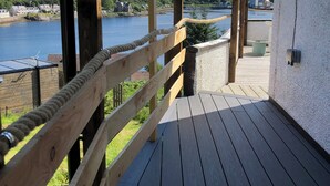 A wooden deck with a view of a lake and houses in the distance. - 2 bed apartment, waterfront views, 5 mins from shops & restaurants (Lochinver)