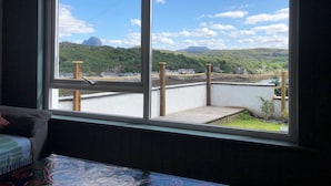 A room with a large window offering a view of a green landscape and a body of water. - 2 bed apartment, waterfront views, 5 mins from shops & restaurants (Lochinver)