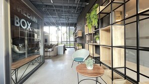 A modern interior with a glass wall labeled "BOX," a seating area with a sofa and chairs, and a wooden table with a plant. - MichiH - Perfeito Studio em Pinheiros (São Paulo)