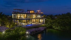 A modern multi-story house with a swimming pool, surrounded by lush greenery and a body of water. - Casa Balam: Private Chef Included - Waterfront Villa - 40ft Pool - Sunset Views (Placencia)