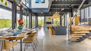 A spacious, modern kitchen with large windows, a dining area with wicker chairs, and a view of greenery outside. - Casa Balam: Private Chef Included - Waterfront Villa - 40ft Pool - Sunset Views (Placencia)