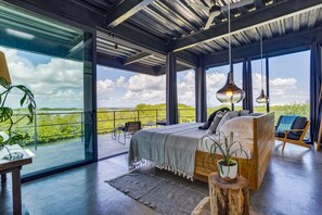 Une chambre moderne avec un grand lit, une vue sur l’extérieur et un balcon équipé de chaises.