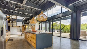 A modern kitchen with a central island, wooden cabinetry, and a large window overlooking greenery. - Casa Balam: Private Chef Included - Waterfront Villa - 40ft Pool - Sunset Views (Placencia)