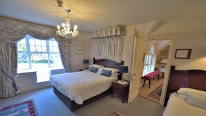 A bedroom with a large bed, a chandelier, a nightstand, and a view of the outside through a window. - Herbert House (Killarney)