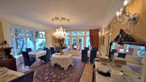 A dining area with a round table, chairs, a chandelier, and a large window with curtains. - Herbert House (Killarney)