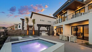 A modern outdoor living area with a pool, patio furniture, and a covered barbecue area.