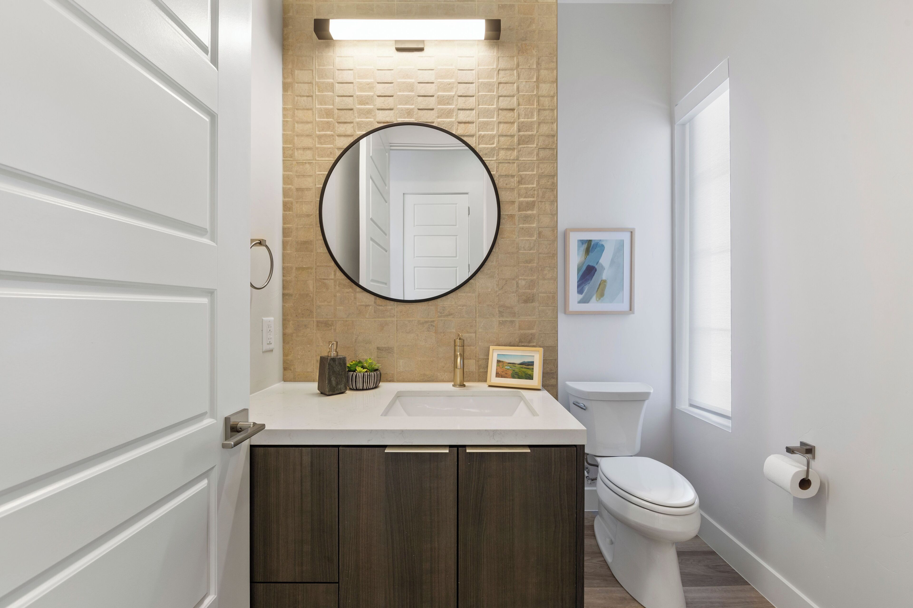 Une salle de bain avec un meuble-lavabo blanc, un miroir rond, des toilettes et une fenêtre.