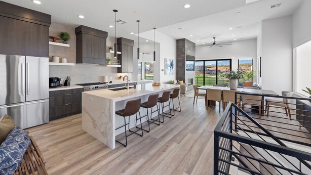 A modern kitchen with a central island, bar stools, and a dining area with a view.