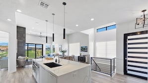 A modern kitchen with a marble island, pendant lights, and a view of the outdoors.