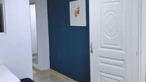 Un pasillo con una puerta blanca, un cuadro en la pared y un banco.
