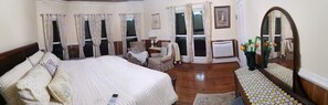 A bedroom with a large bed, a sitting area with a chair and table, and a mirror reflecting the room.