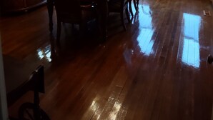 Une salle à manger avec une table en bois, des chaises, un lustre et une vue dégagée sur l’extérieur grâce à de grandes fenêtres.