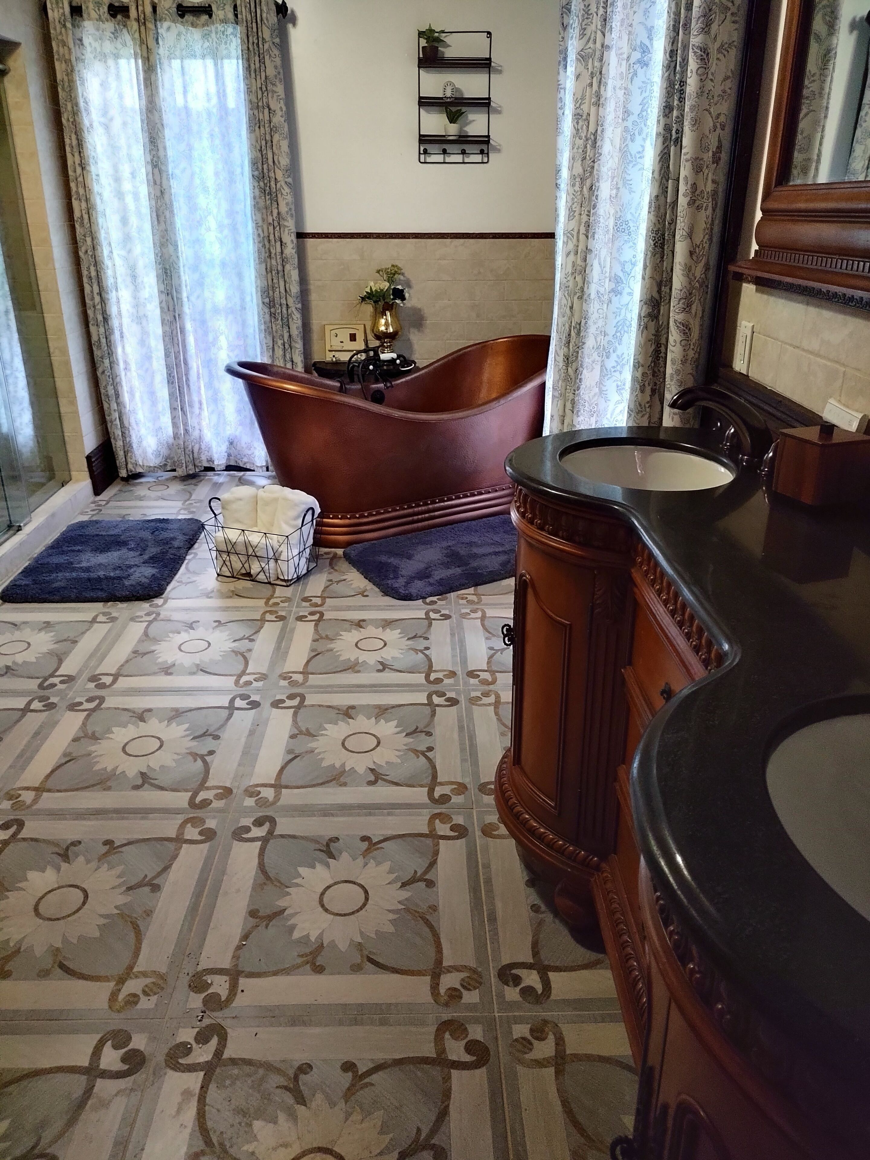 Une salle de bain avec une baignoire sur pieds, un meuble-lavabo en bois avec un évier noir, des carreaux de sol à motifs et une étagère murale agrémentée d’objets décoratifs.