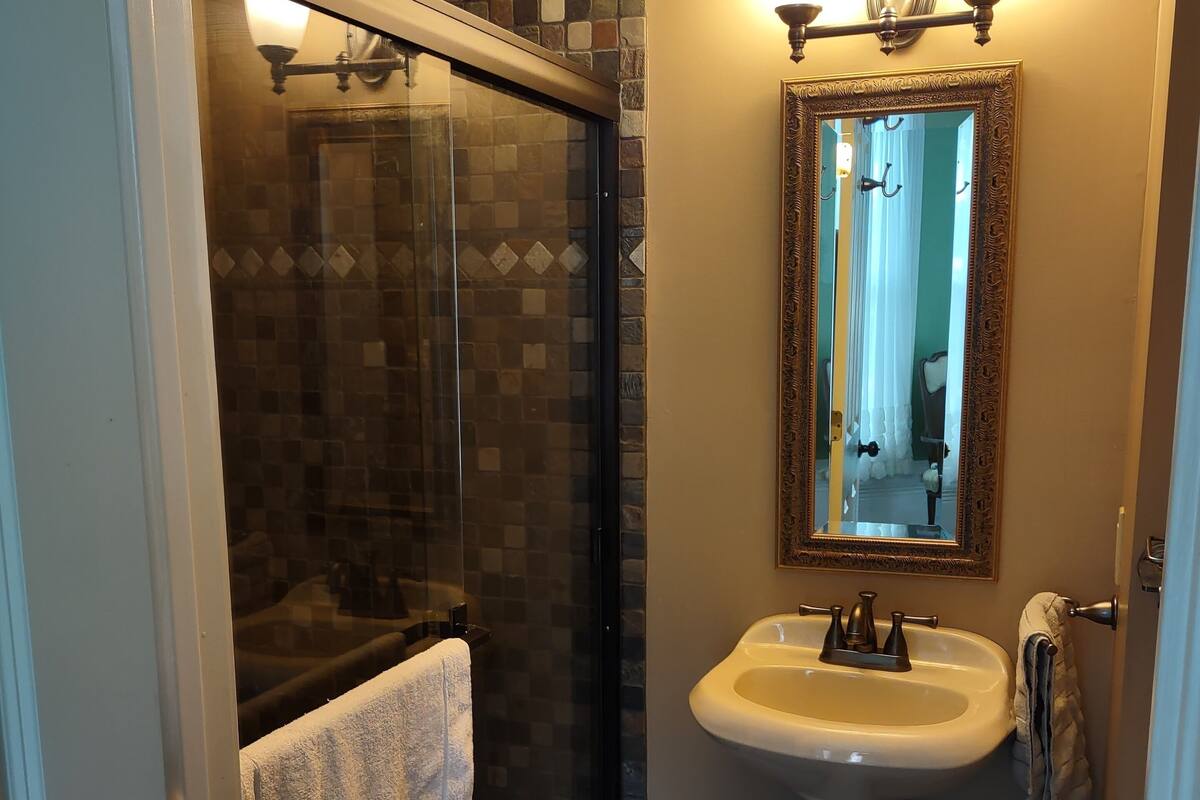 Une salle de bain dotée d’une douche à parois de verre, d’un lavabo sur colonne et d’un miroir avec un cadre décoratif.