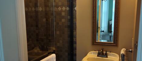 A bathroom with a glass shower enclosure, a pedestal sink, and a mirror with a decorative frame.