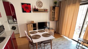 A modern kitchen with red cabinets, a dining area with a white table and chairs, and a living room with a large window and curtains. - Mare Verde A10 (Costa Adeje)