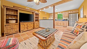 Amplia sala de estar con armarios de madera, televisor, sofá con cojines estampados y ventilador de techo.