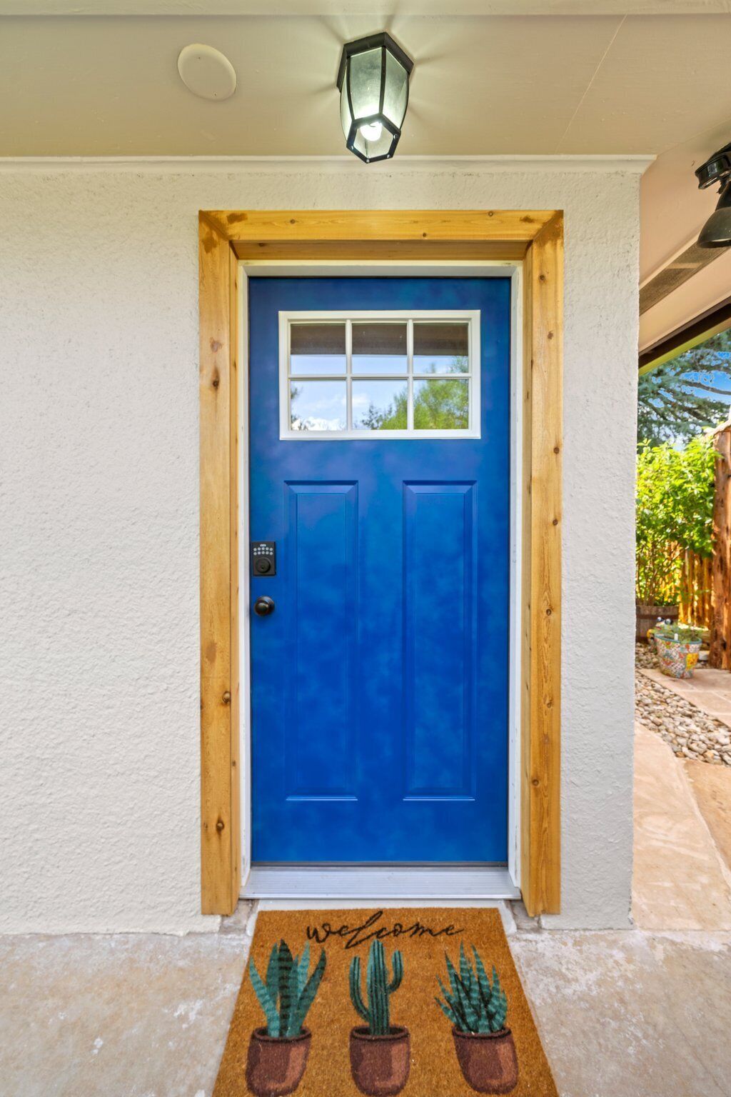 Una porta blu con una finestra sopra, stipite in legno e tappeto d'ingresso con motivi di cactus.