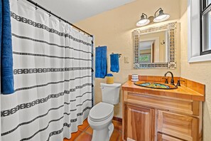 Une salle de bain avec un rideau de douche, des toilettes, un lavabo avec un miroir et une fenêtre.