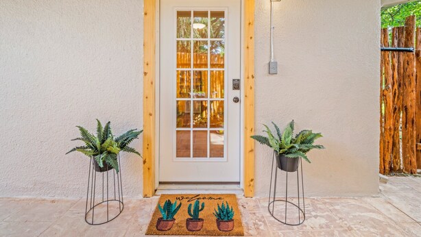 Puerta principal con panel de vidrio, dos macetas a cada lado y felpudo con dibujos de cactus.