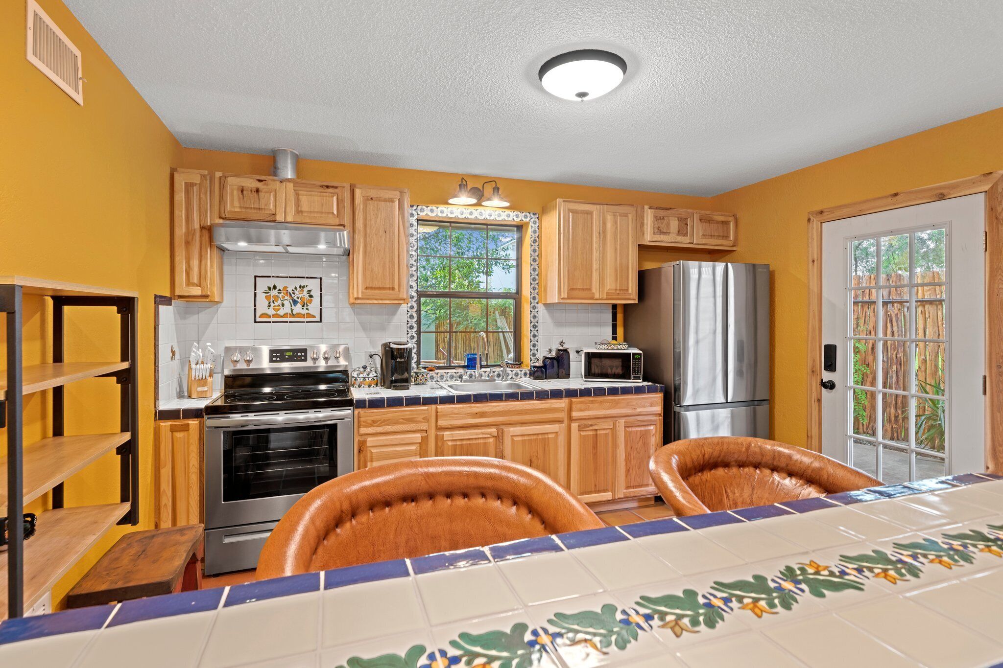 A kitchen with wooden cabinets, a stainless steel refrigerator, a microwave, and a large window.