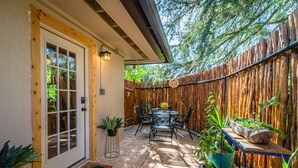 Un patio con una mesa y sillas, rodeado por una valla de madera y plantas en macetas.