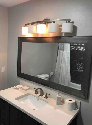 A bathroom with a large mirror, a sink, a toilet, and a shower curtain.