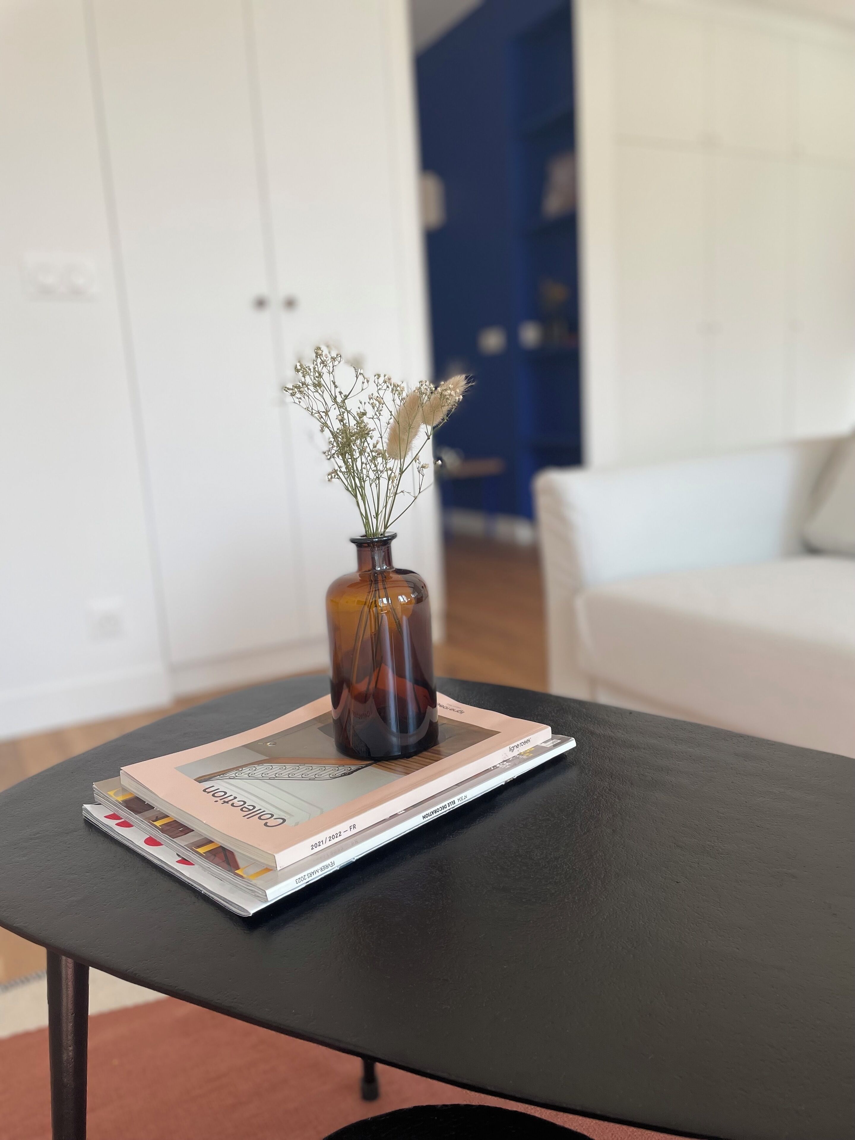 A black coffee table with a magazine and a vase with dried flowers.